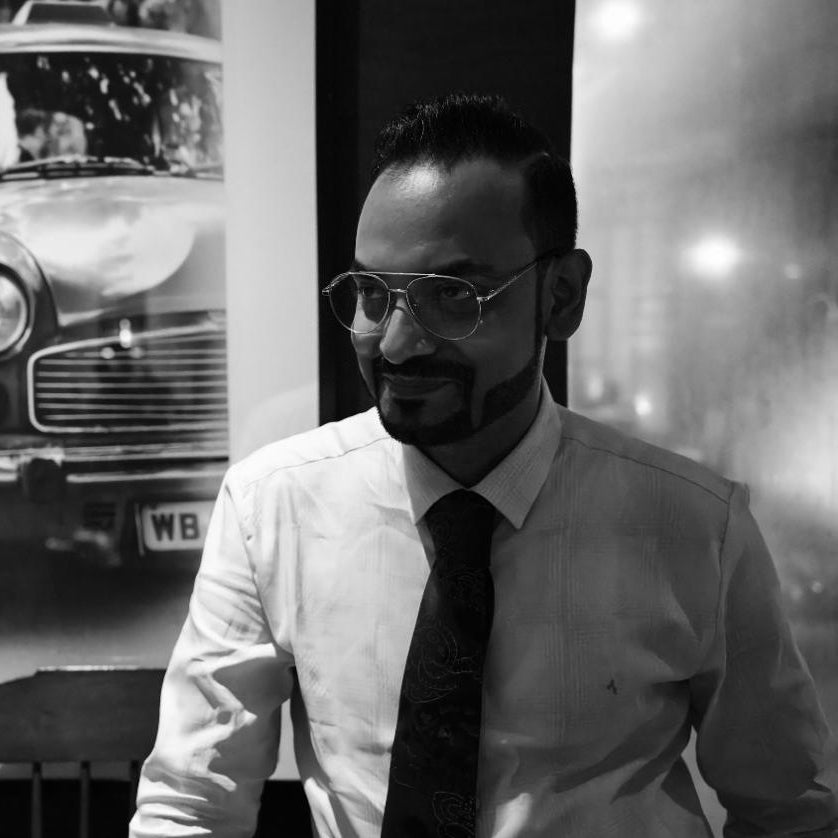 Man wearing glasses and a tie in front of a vintage car display